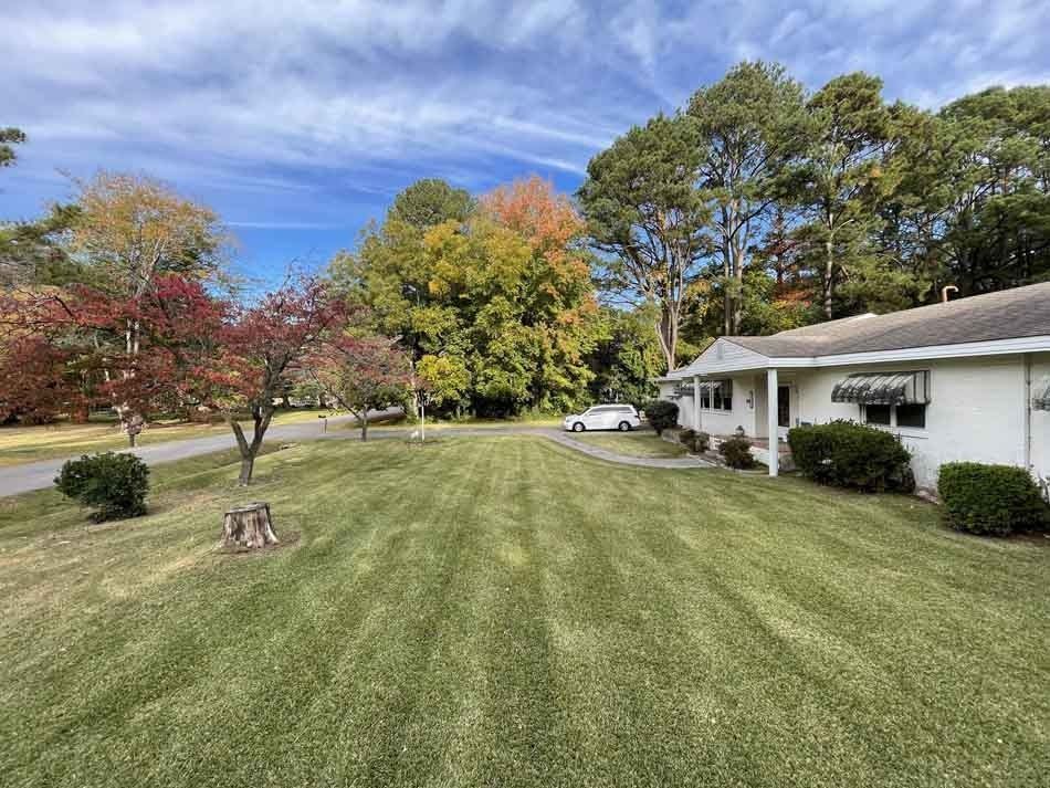 A well-manicured lawn leads to a white house with trees in fall foliage under a blue sky.