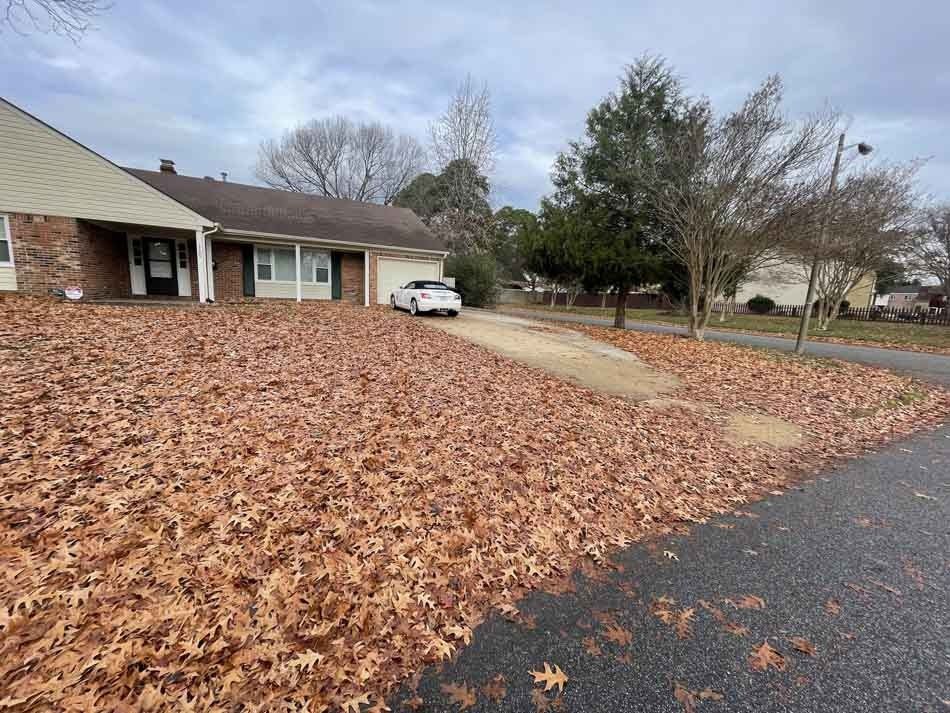 A residential house with a driveway covered in fallen brown leaves; a white car parked there.