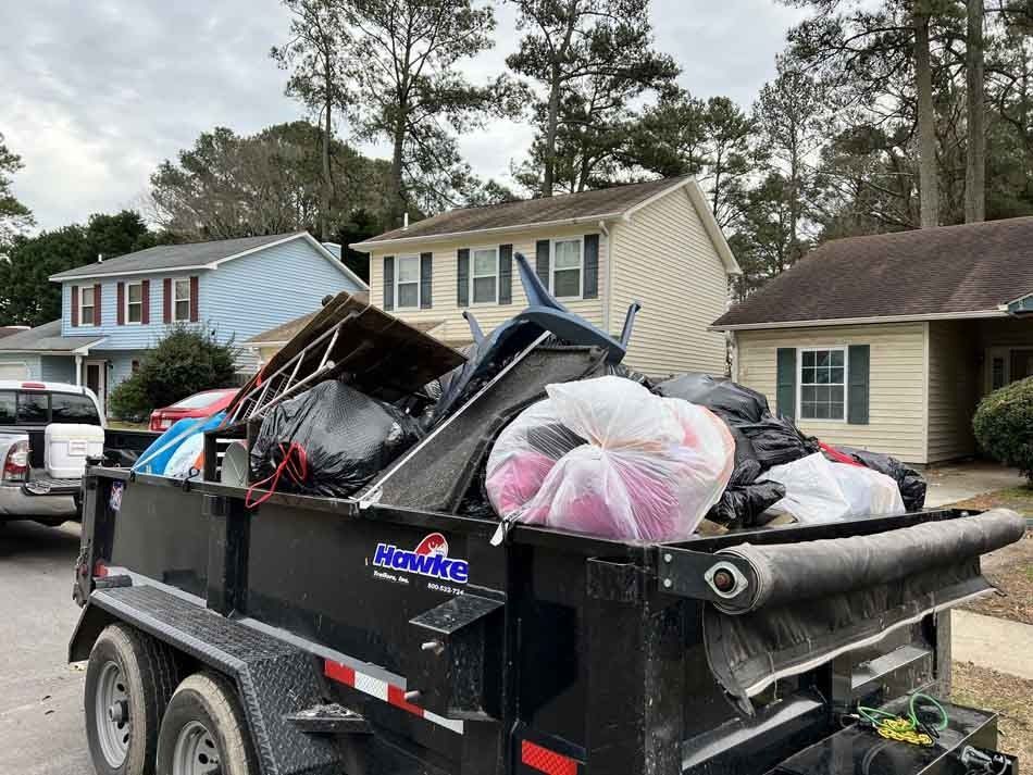 A trailer overflowing with trash parked in a residential neighborhood with houses and trees.