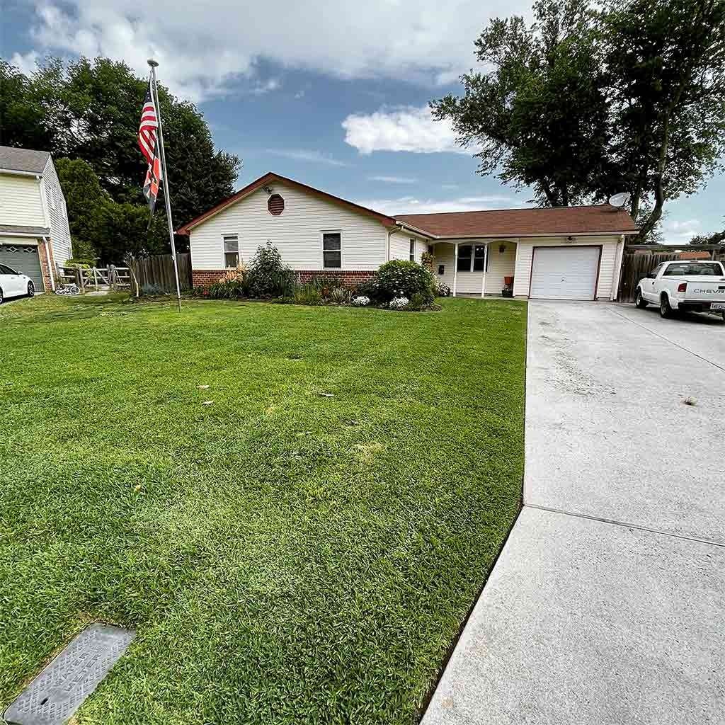 A beige house with a green lawn, American flag, and a white garage door. A white truck is parked nearby.