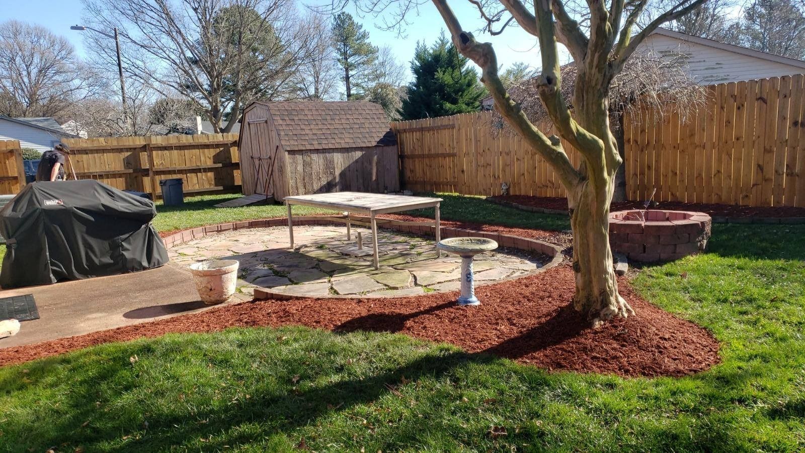 Backyard with shed, patio, fire pit, and tree, surrounded by a wooden fence.
