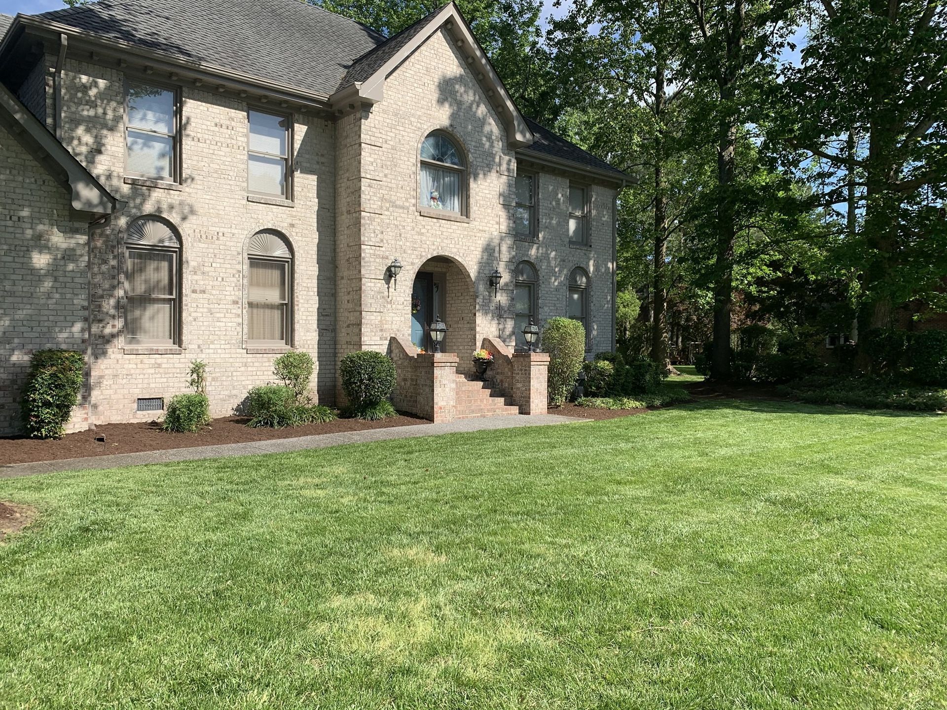 Two-story brick house with green lawn and landscaping under a sunny sky.