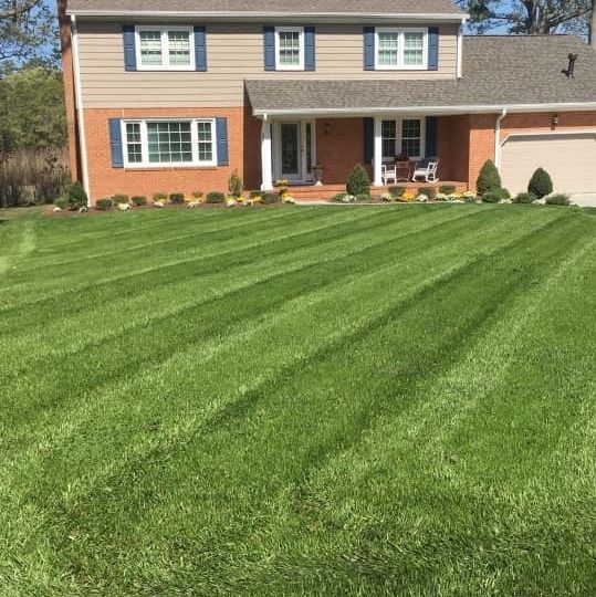 Well-manicured lawn in front of a two-story brick house with blue shutters.