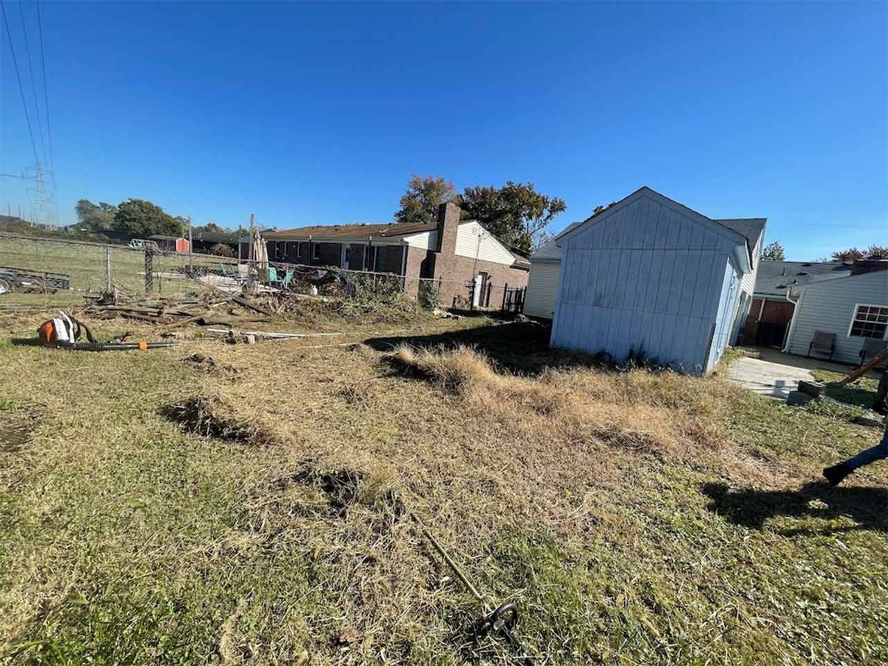 Debris-strewn field with damaged buildings under a clear blue sky.
