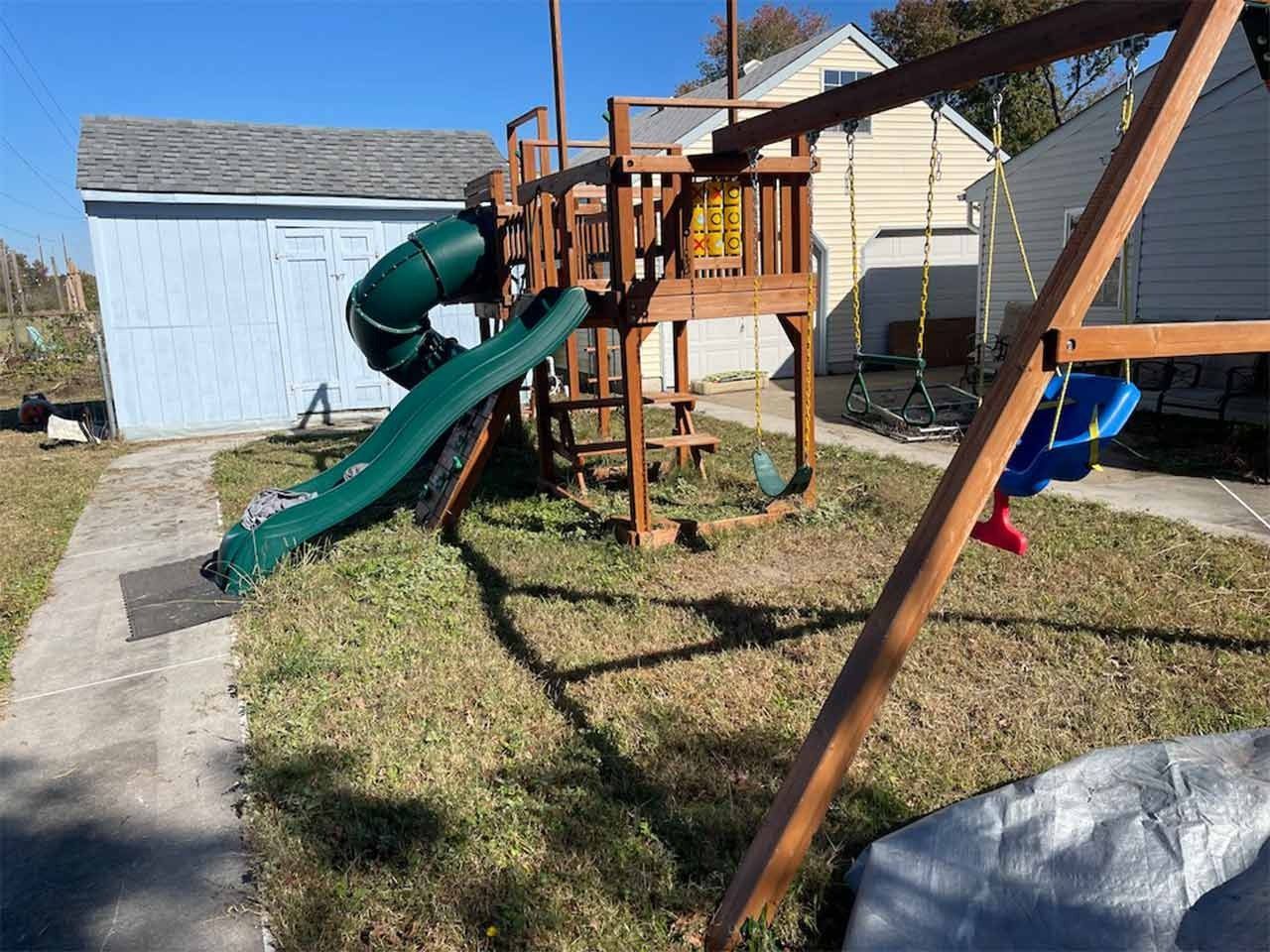 Wooden playground set with slide, swings, and stairs in a grassy yard.