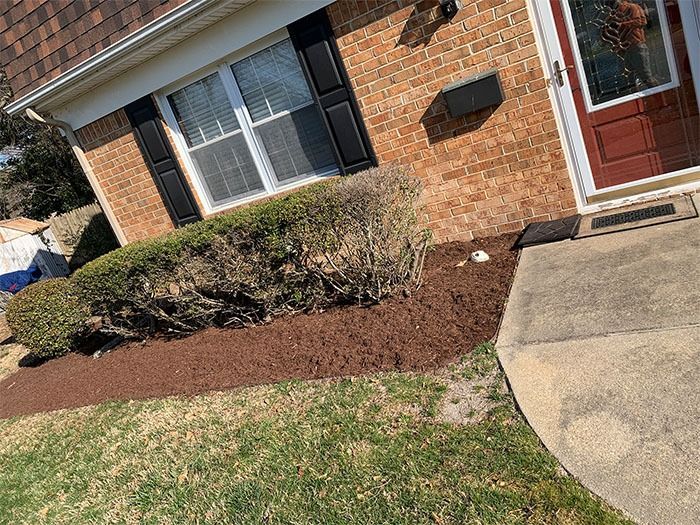 House exterior with a brick facade, door, window, and freshly mulched garden bed.