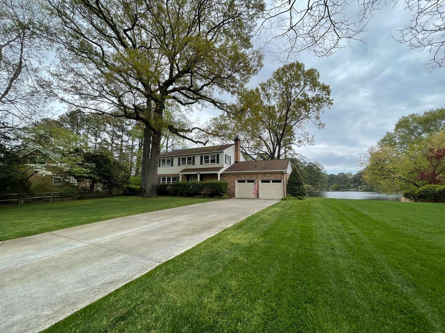 Two-story house with a long driveway, two-car garage, and lush green lawn on a cloudy day.