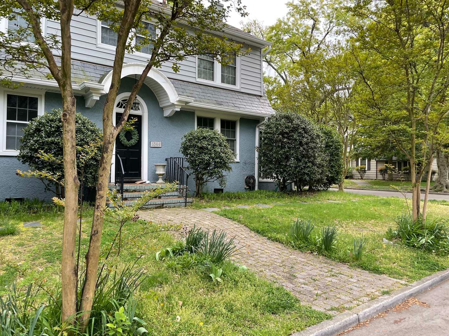 Blue house with a gray roof and a stone path leading to the front door, surrounded by trees and bushes.
