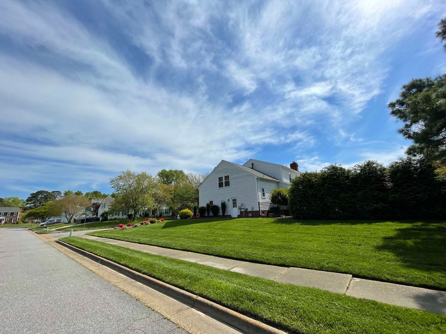 White house with green lawn on a sunny day with a blue sky and streaky clouds.