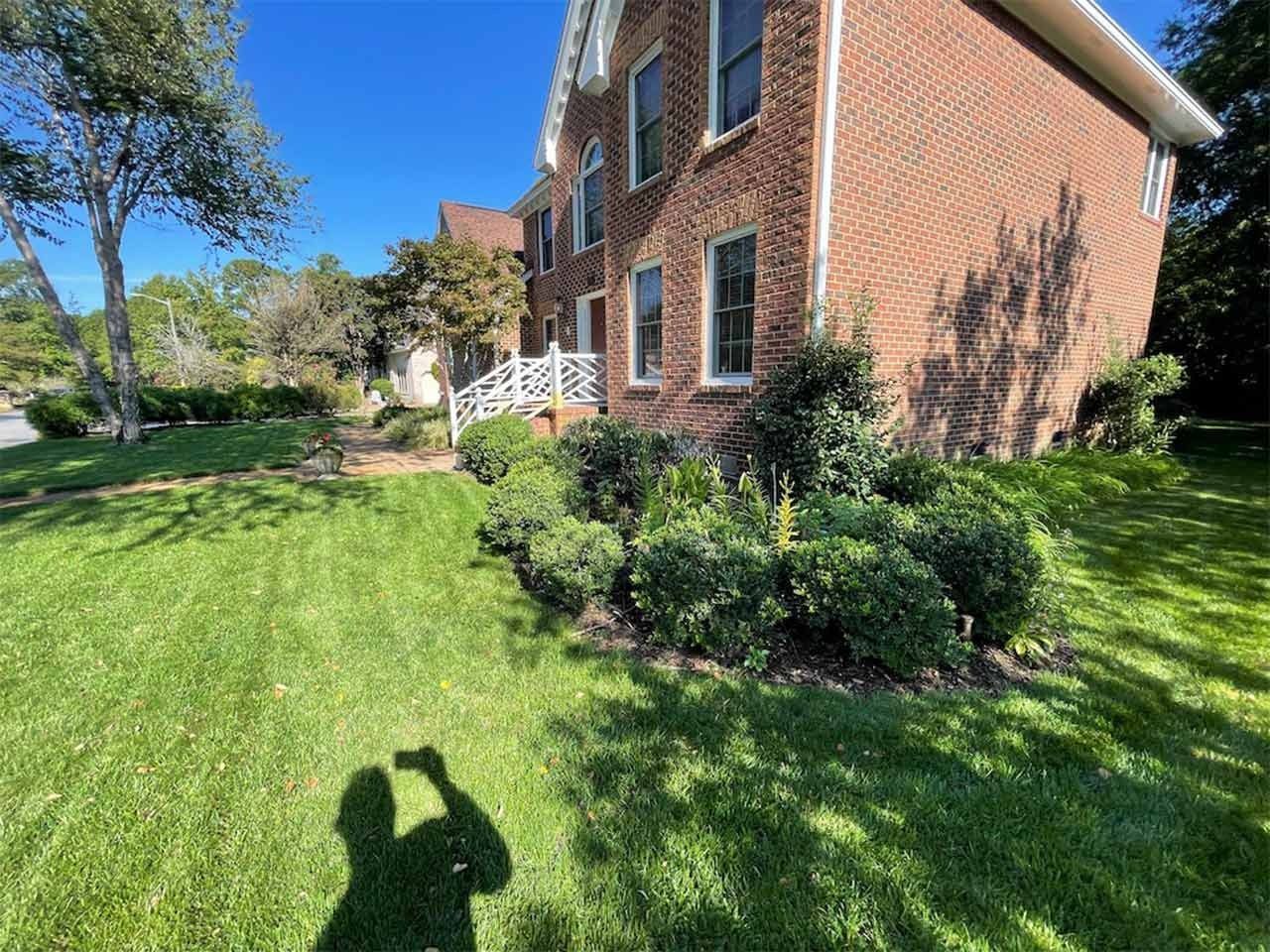 Brick building with green lawn and bushes. Shadow of person taking the photo. Sunny day.