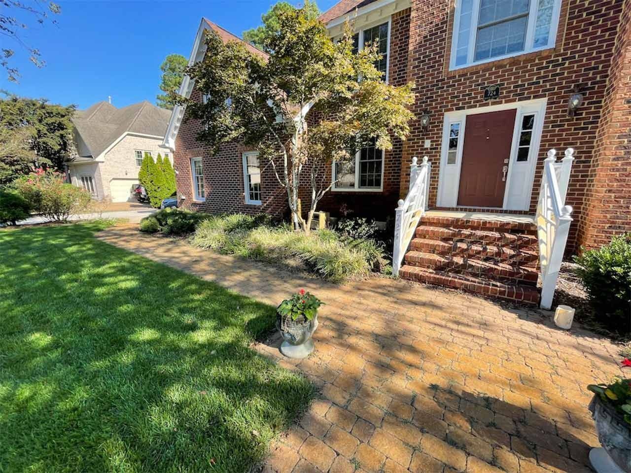A brick home with a pathway leading to the front door. Landscaping includes grass, shrubs, and trees.