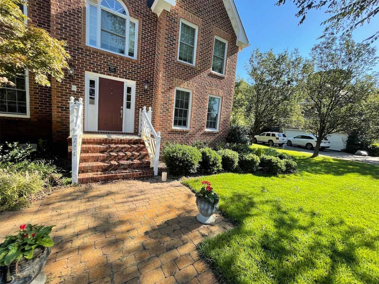 Red brick house with a walkway, steps, and landscaping on a sunny day.