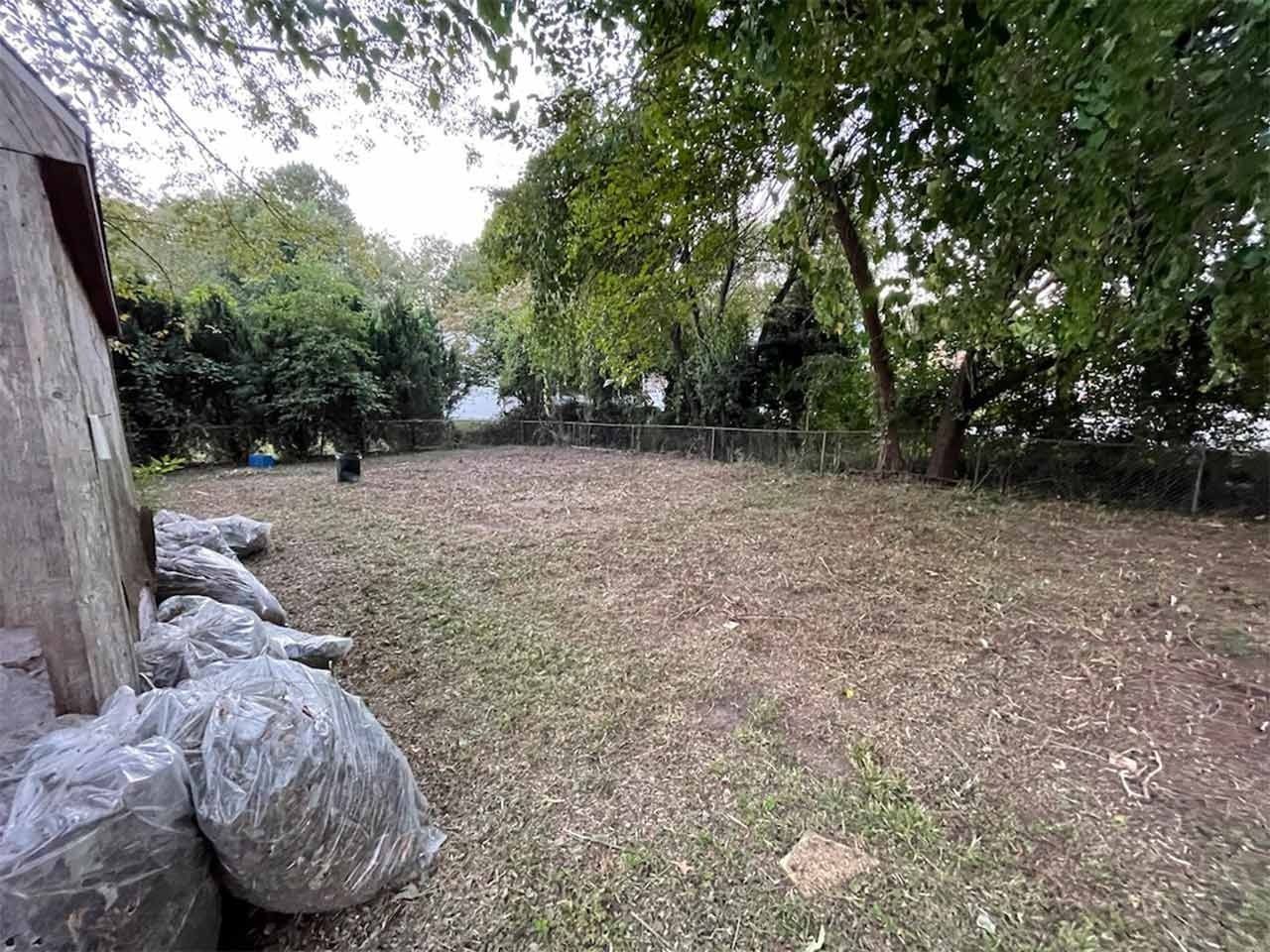 Backyard with bags of debris, cleared of grass. Trees in the background. Overcast day.