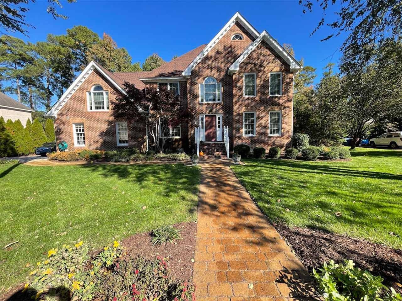 Brick house with green lawn, brick walkway leading to the front door, blue sky.