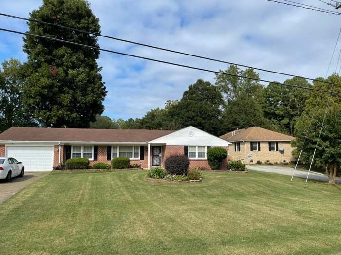 Ranch-style house with brick and a white garage, green lawn, and trees on a cloudy day.