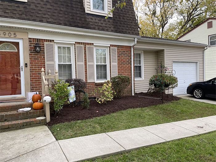 Brick house with a small yard, mulch, shutters, and a garage. Pumpkins by door.