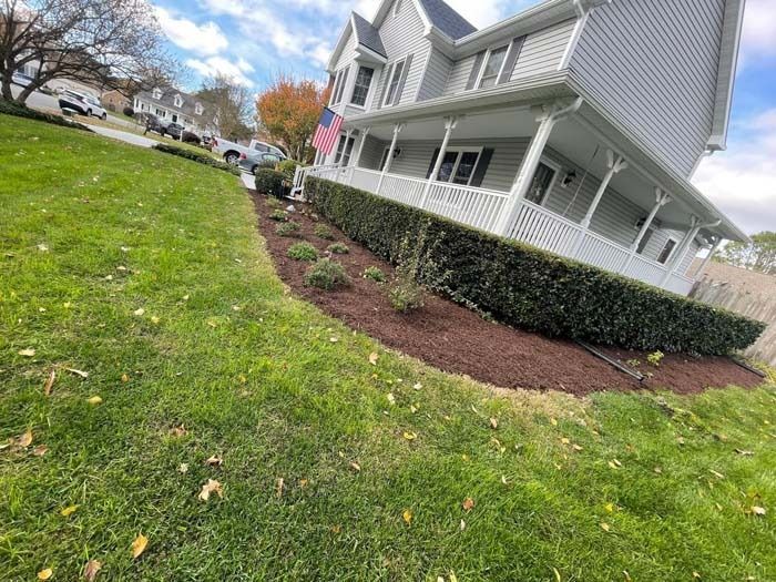 House with a long, neatly trimmed hedge and freshly mulched garden bed on a sloped lawn.