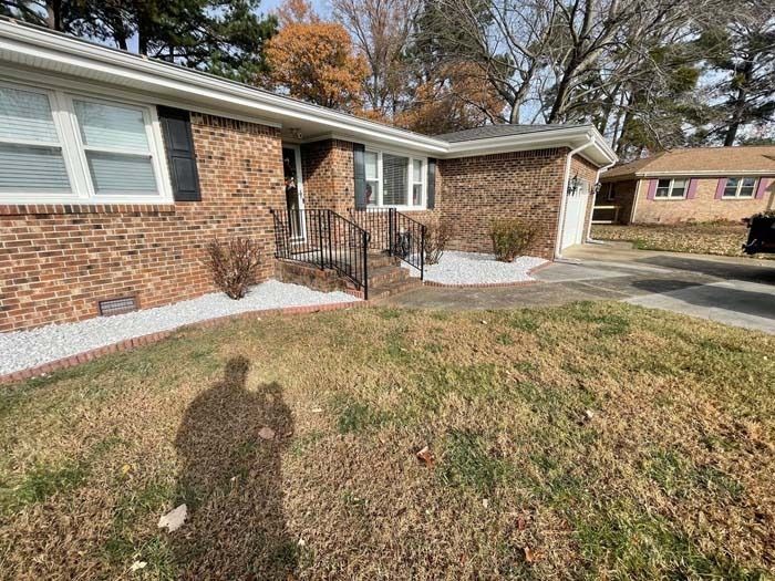 Brick house with white gravel border, black shutters, and brown lawn.