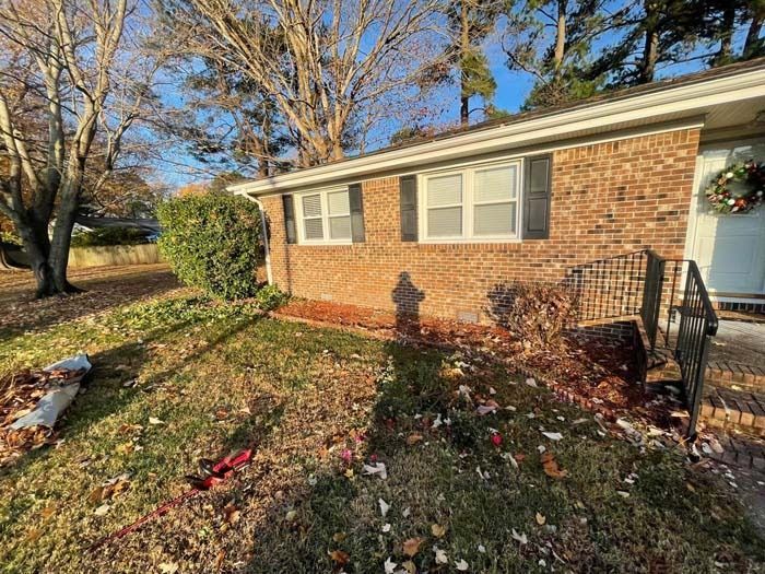 Brick house exterior with small windows, black shutters, and brown landscaping. Sunny day.