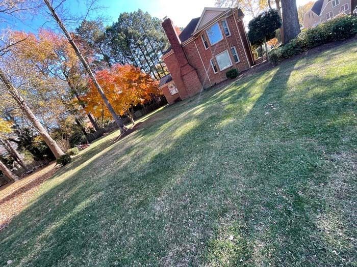 A house with a red brick chimney on a grassy lawn with autumn trees and a blue sky.
