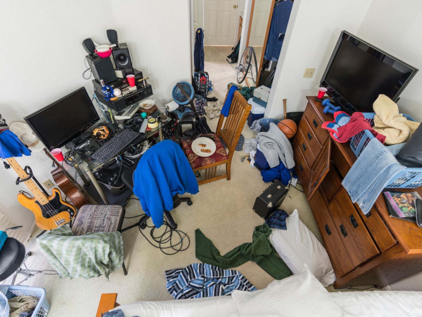 Cluttered bedroom: desk with computer, guitar, dresser with clothes, trash, and various items scattered on the floor.