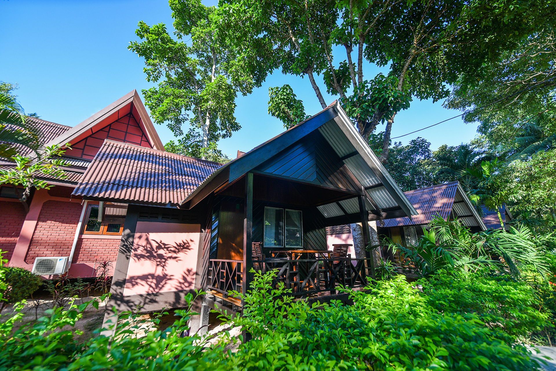 Brown bungalows nestled in lush green foliage under a blue sky.