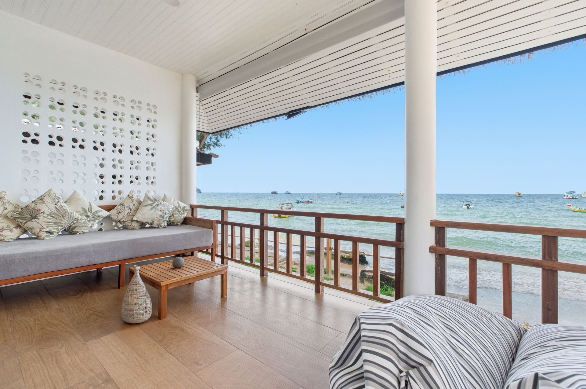 Beachfront veranda with wood flooring, couch, ocean view, and wooden railing.