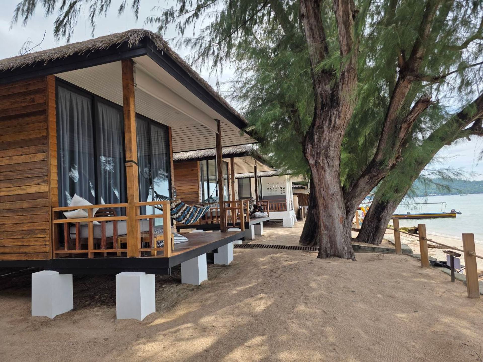 Wooden beachfront bungalows with thatched roofs and a sandy beach.