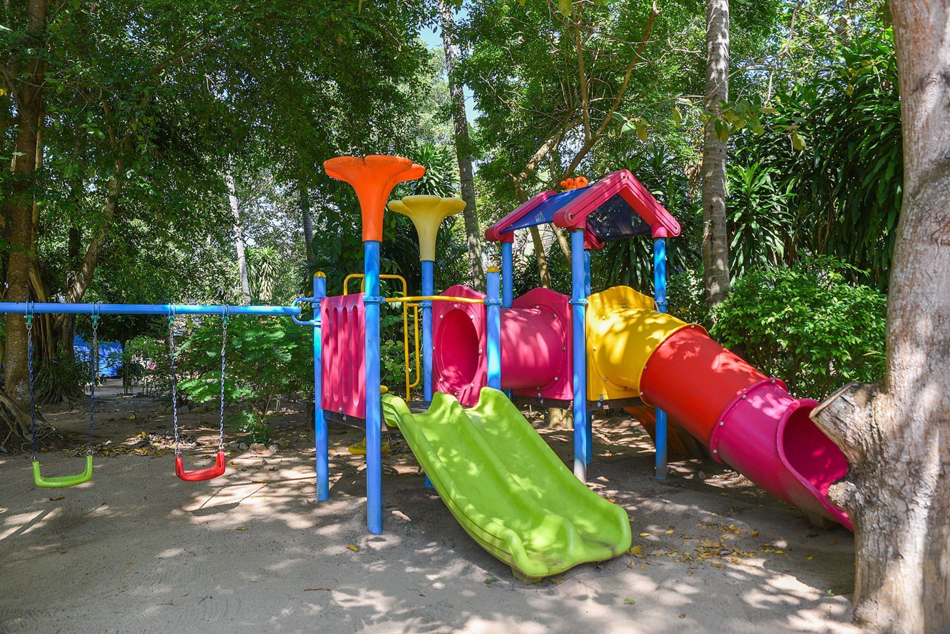 Colorful playground set with slide, tunnel, and swings in a wooded area.