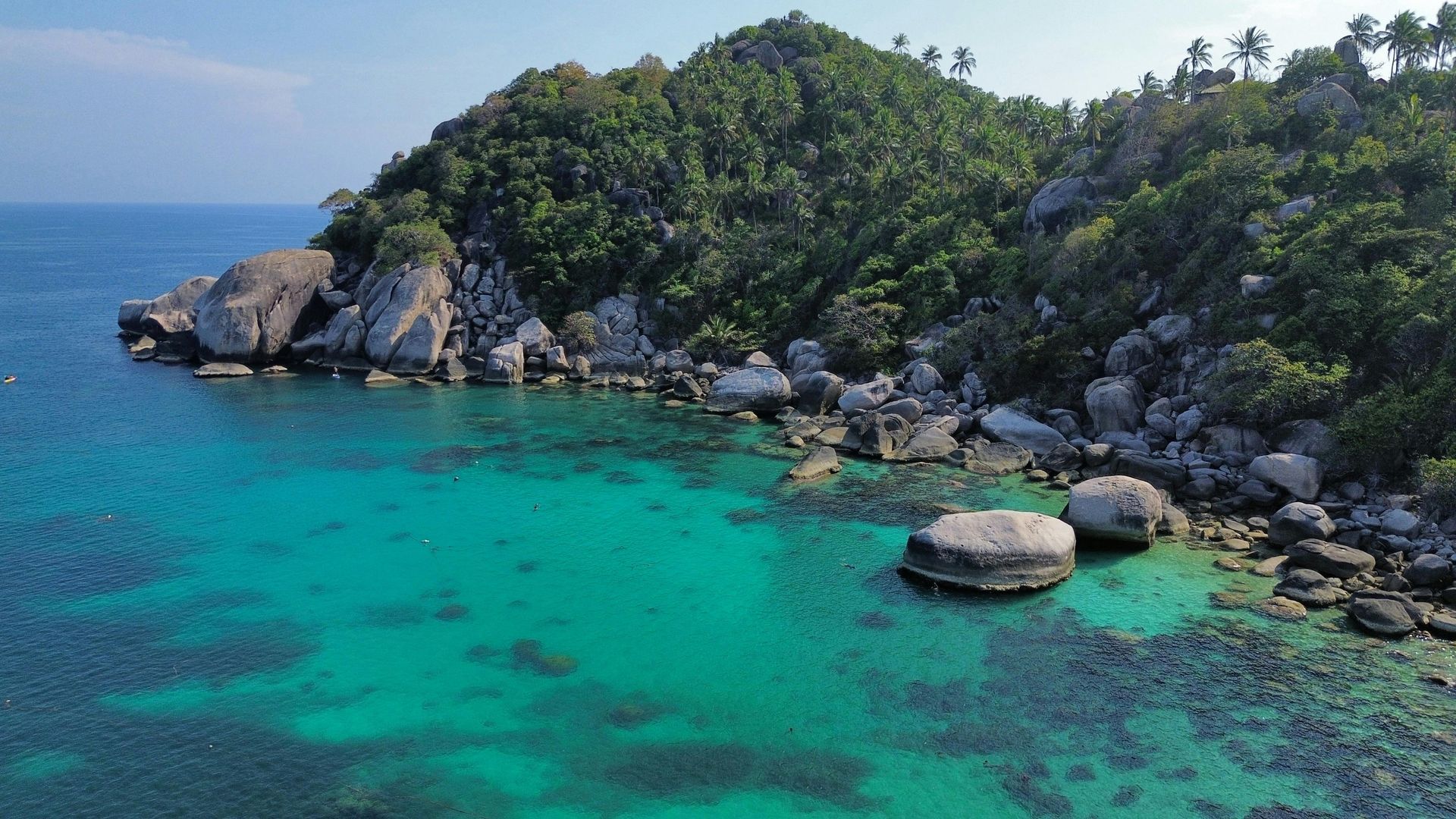 Rocky coastline with turquoise water, lush green hillside, and large boulders.