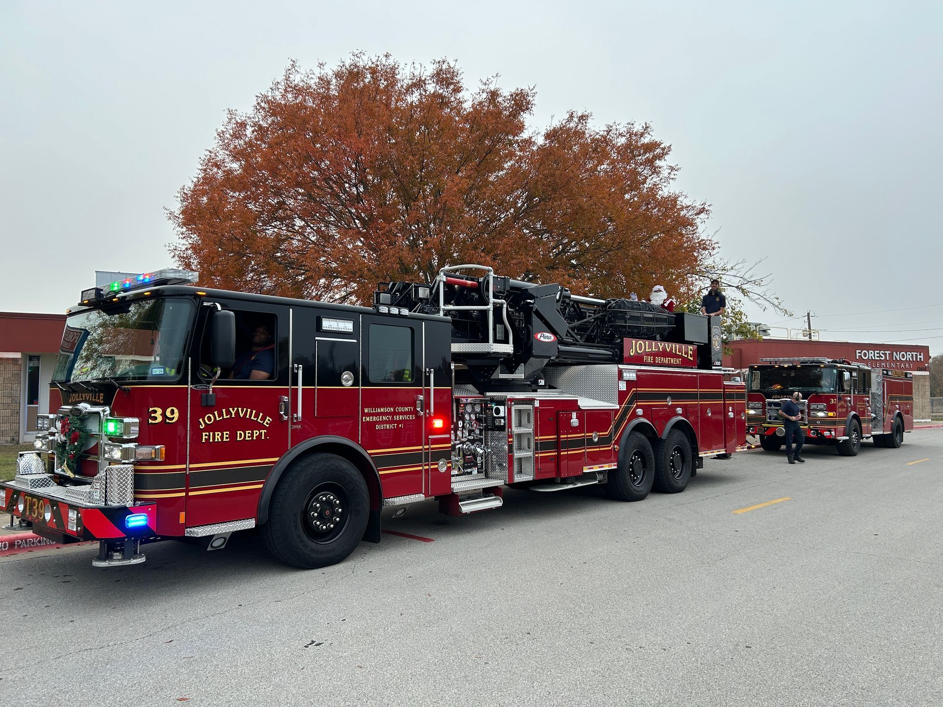 A red fire truck and a smaller black vehicle parked near a building. Fall foliage in the background.