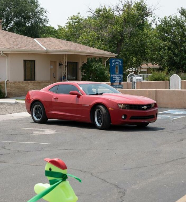 A red sports car is parked on a paved area near a beige building.