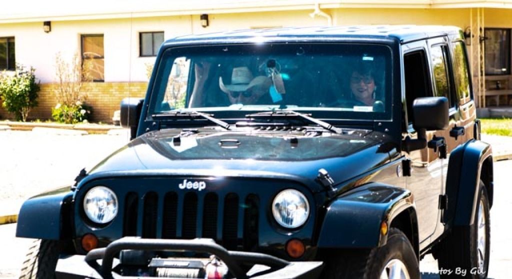 A black Jeep is parked outdoors, with two smiling individuals inside. 