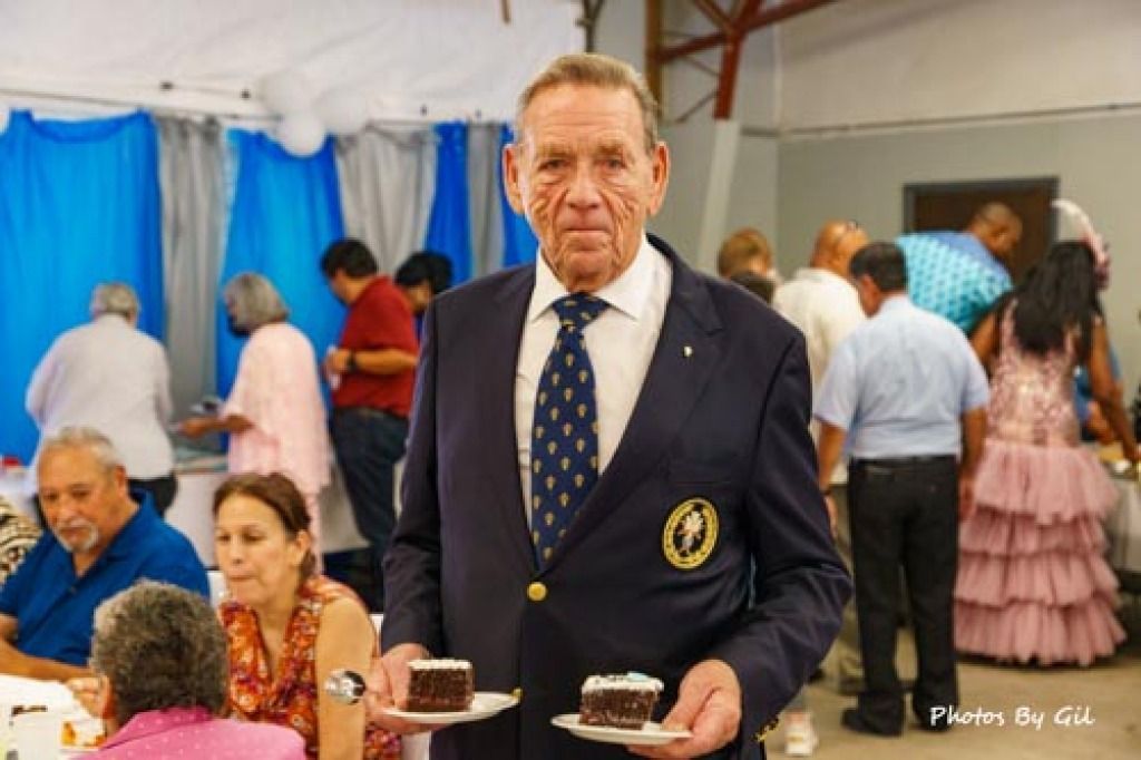 Elderly man in a suit holding two plates of chocolate cake.