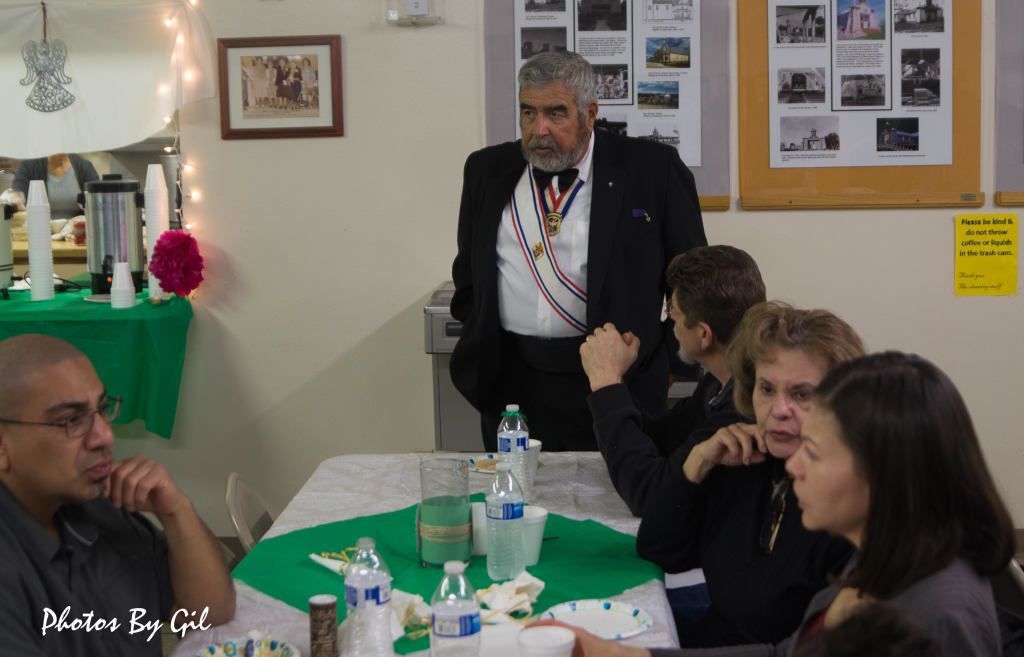 A man in formal attire with a medallion stands near a table. 