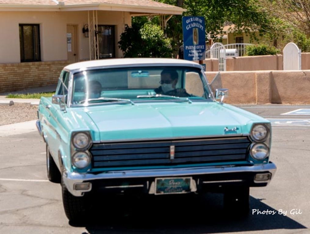 A classic turquoise car with chrome details is parked in front of a beige building. 