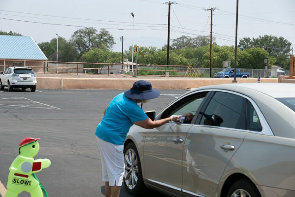 A person wearing a blue shirt and hat leans into a white car window in a parking lot.