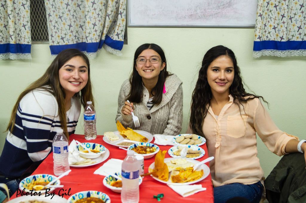Three women sit at a table with red tablecloth, smiling.
