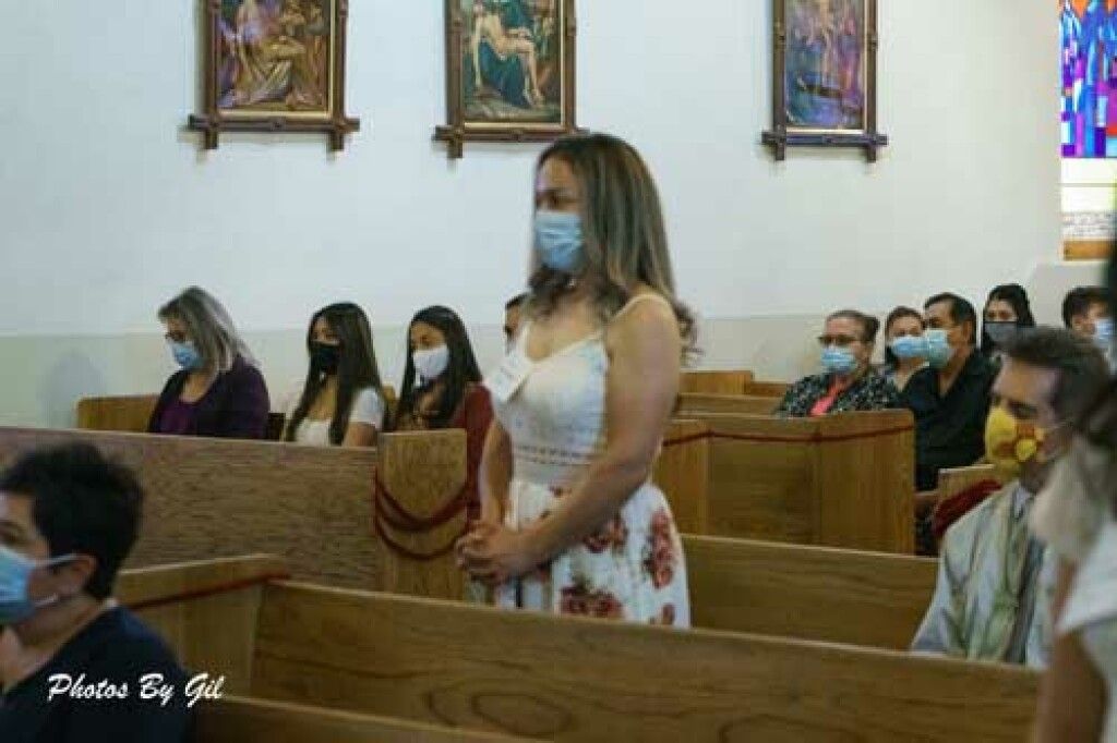 A woman in a floral dress and face mask stands in a church pew.