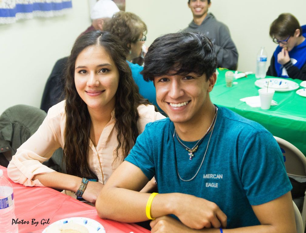 A young woman and man smile at a table with a red tablecloth.