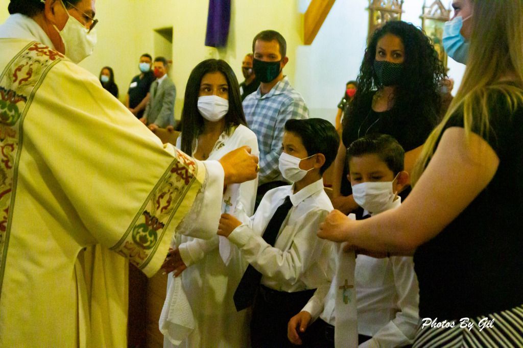 A priest in ornate robes interacts with masked children dressed in white and black during a church ceremony. 