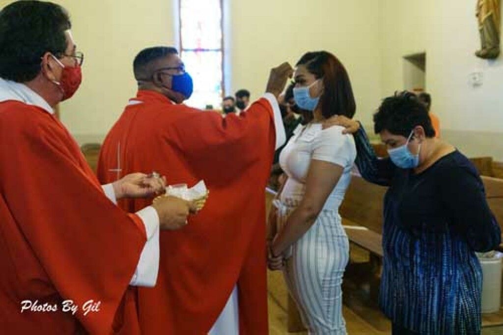 A priest in a red robe performs a ritual on a woman in a church. 