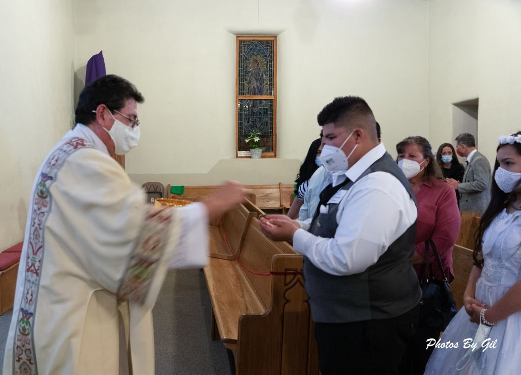 A priest in robes and a mask gives communion to a masked congregant in a church. 