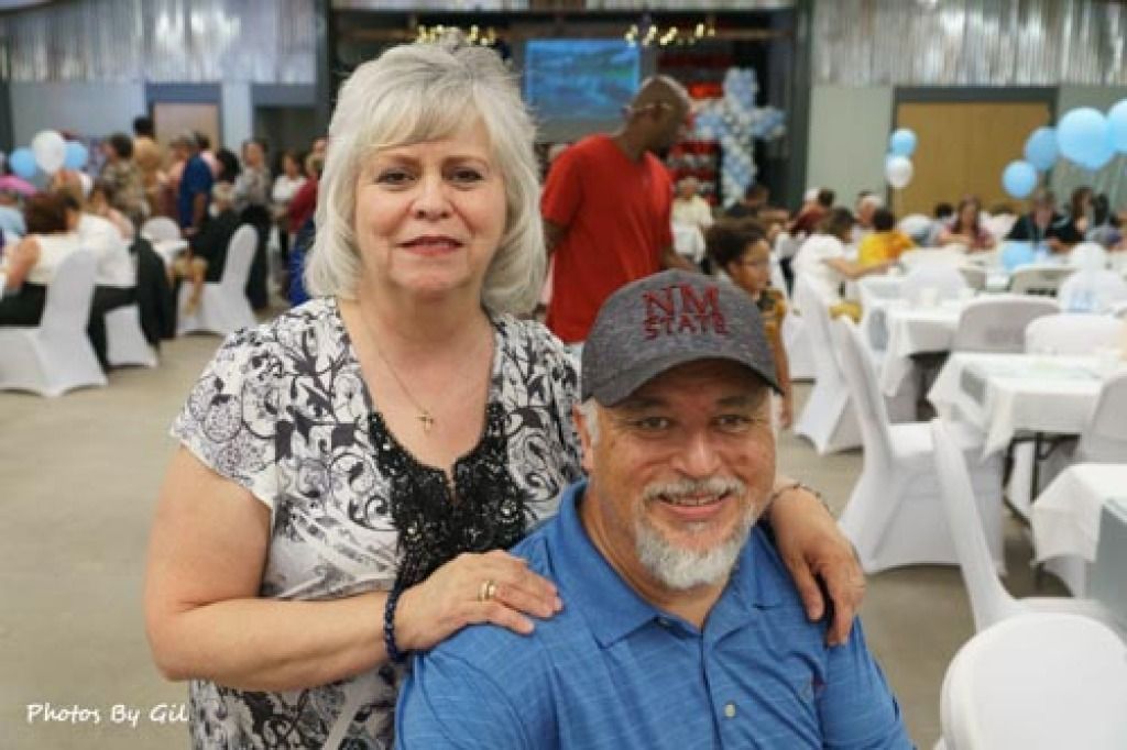 Smiling older couple poses in a decorated banquet hall with white tablecloths and balloons. 