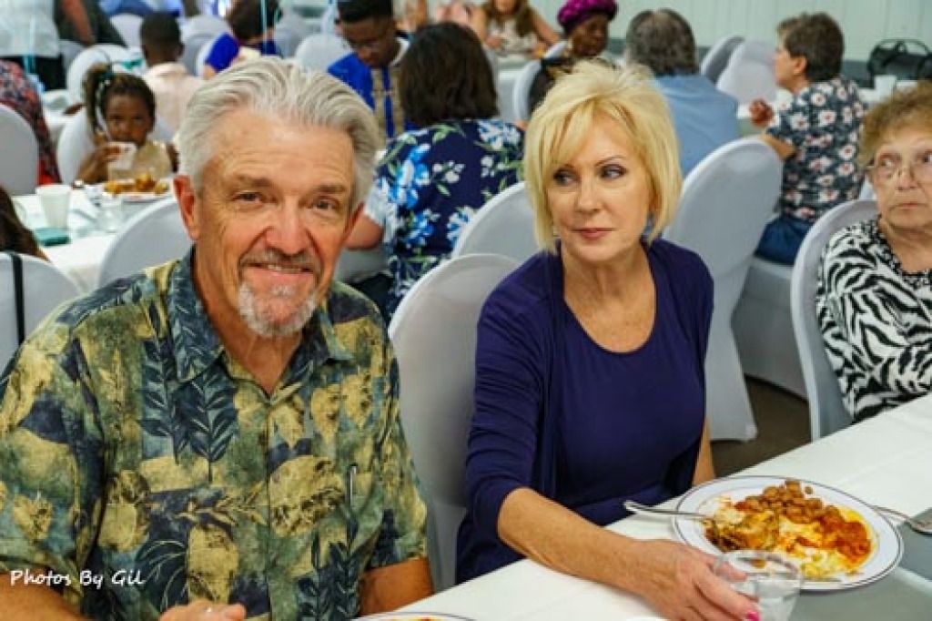 A mature couple sits at a dining table with a plate of food. 