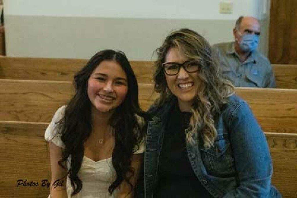 Two women sit smiling on wooden benches.