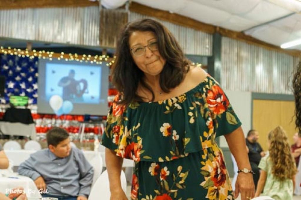 A woman in a floral dress smiles warmly at a gathering. 