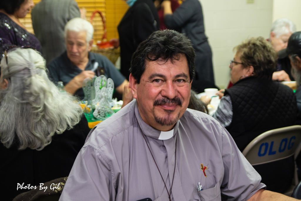 Priest smiling warmly at a gathering, wearing a clerical collar.