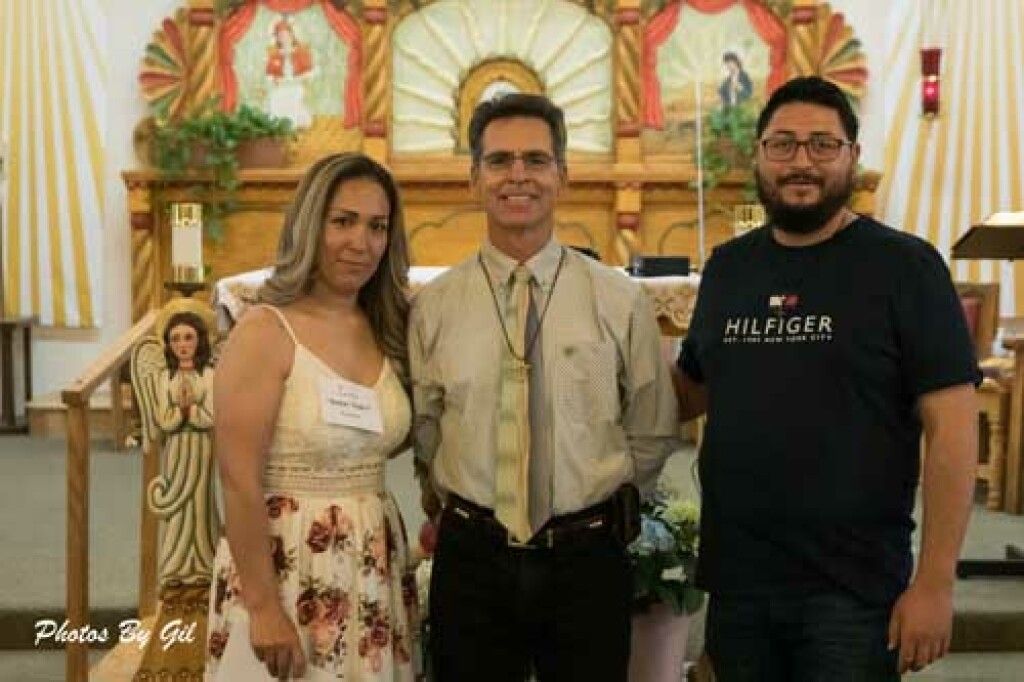 A group of three people stand smiling inside a brightly decorated church. 