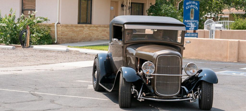 A classic vintage car with a shiny metallic finish and chrome details is parked in a lot. 